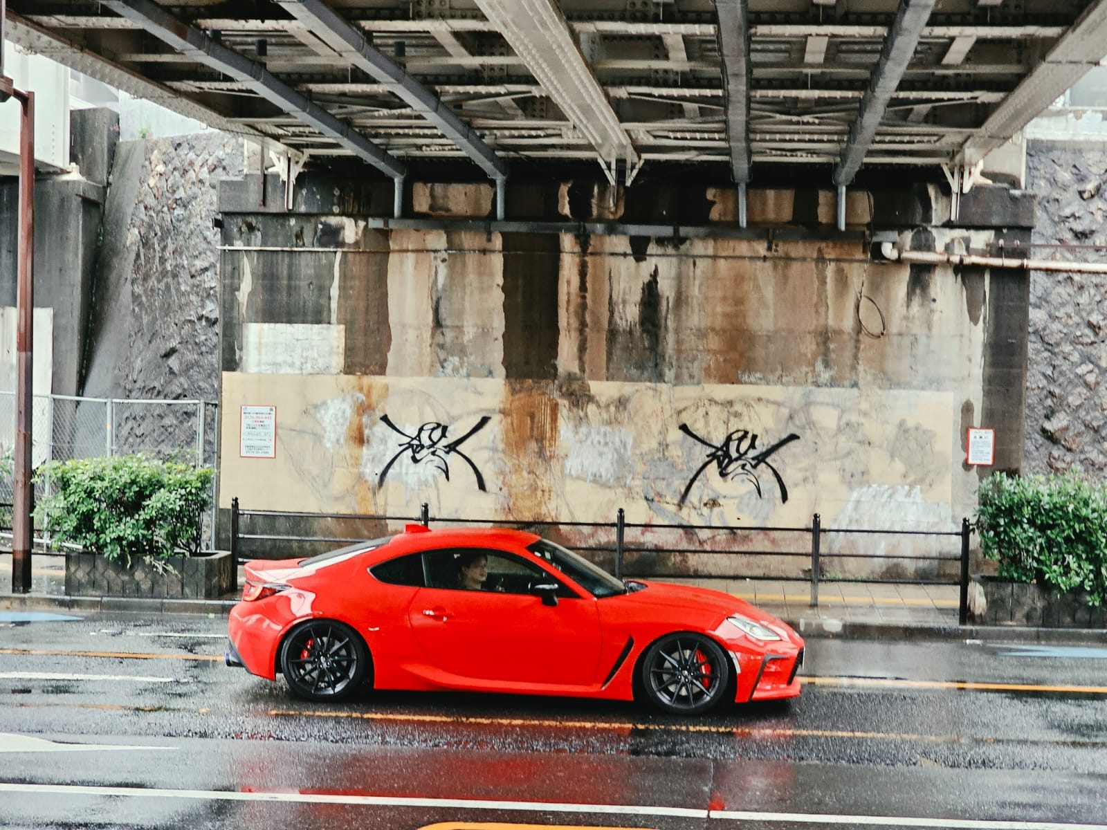 A red Toyota GR86 driving through rain beneath an overpass