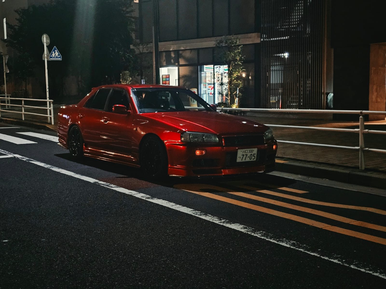 Red Nissan Skyline ER34 sedan parked at night near a convenience store in Kawaguchi
