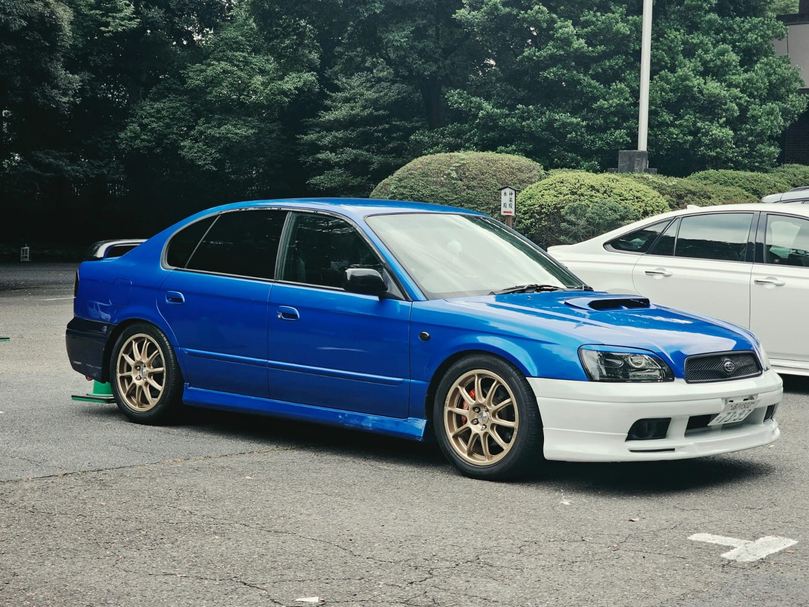 Blue and white Subaru Legacy B4 with gold wheels parked near a shrine