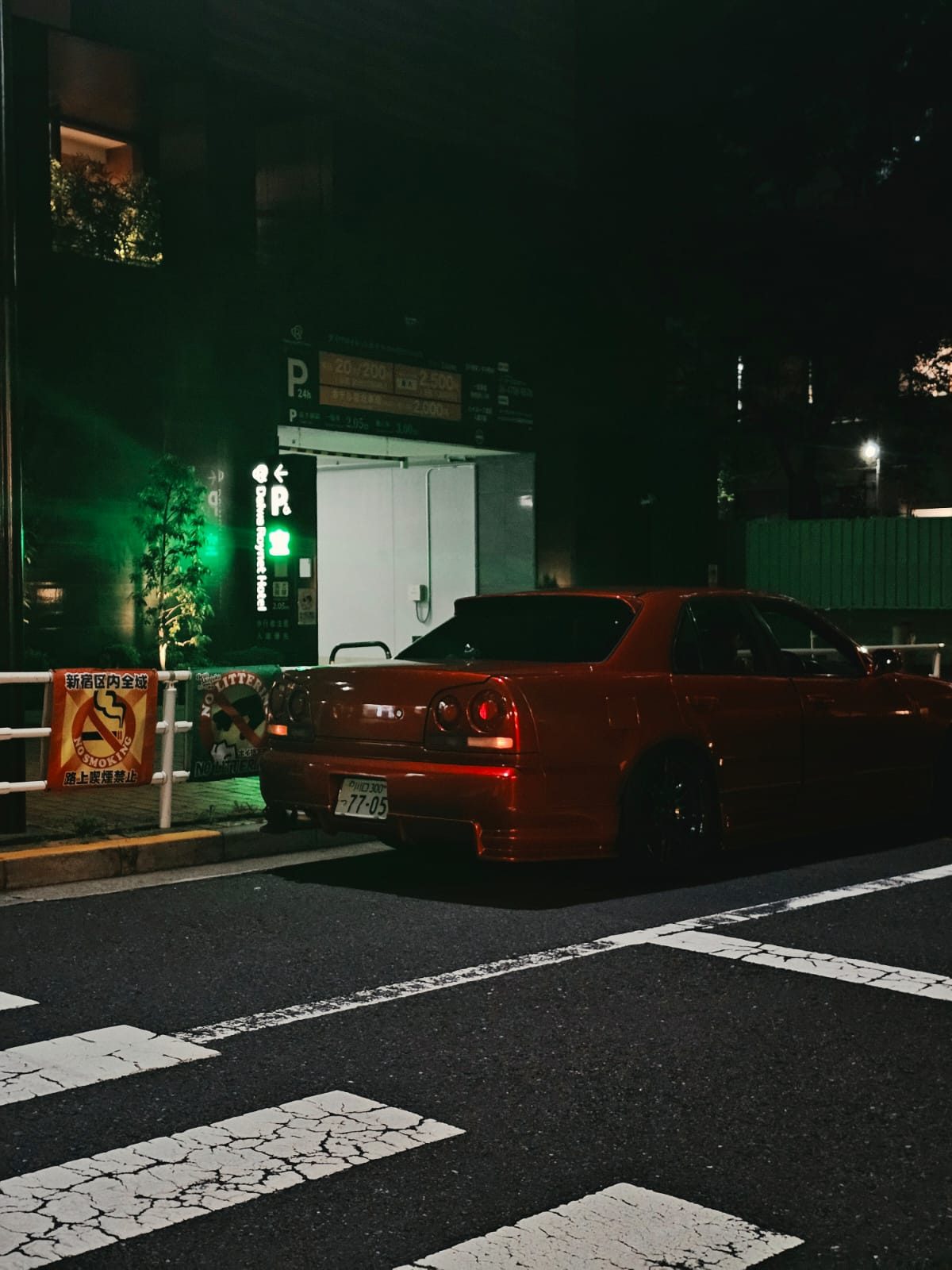 Red Nissan Skyline ER34 sedan at night under a green streetlight
