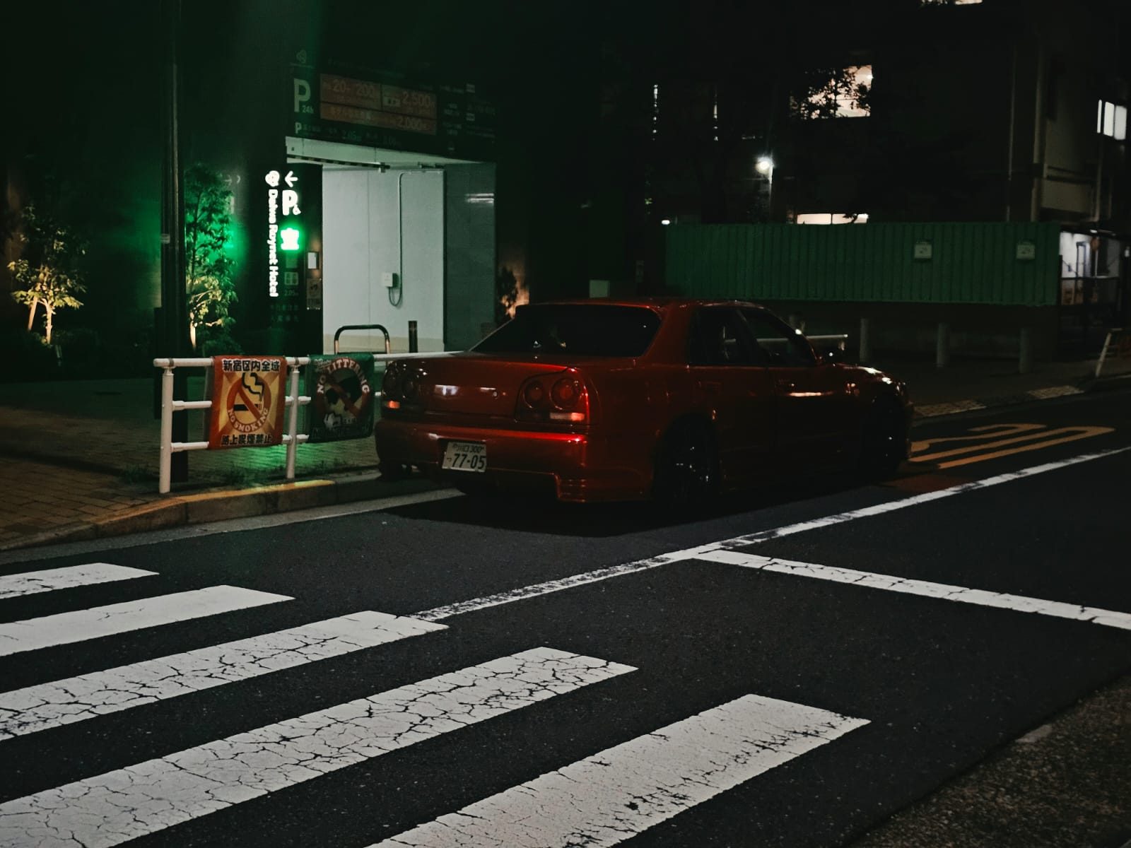 Red Nissan Skyline ER34 sedan at night near a hotel entrance