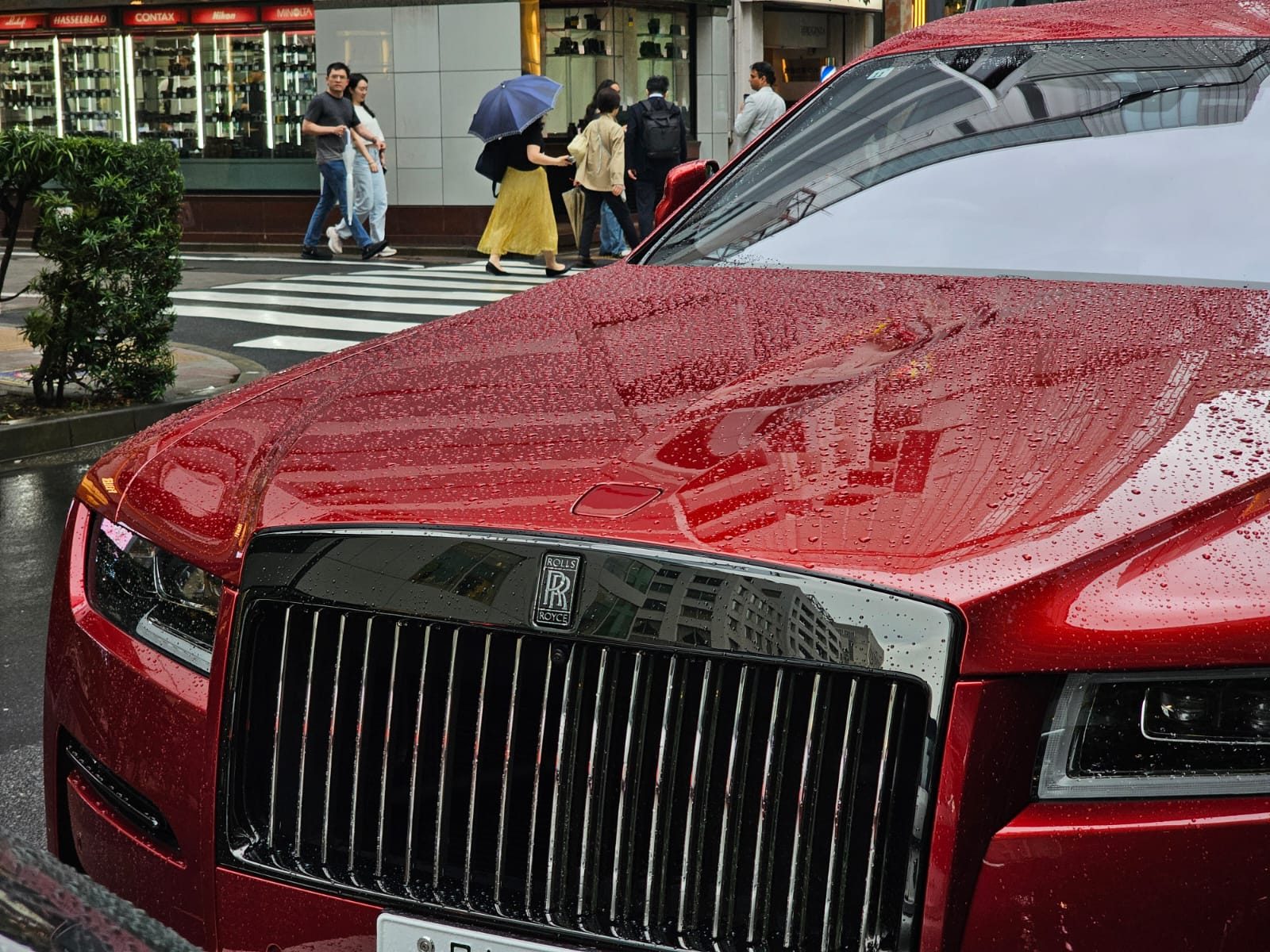 Red Rolls-Royce Ghost grille in the rain, with Ginza camera shops in the background