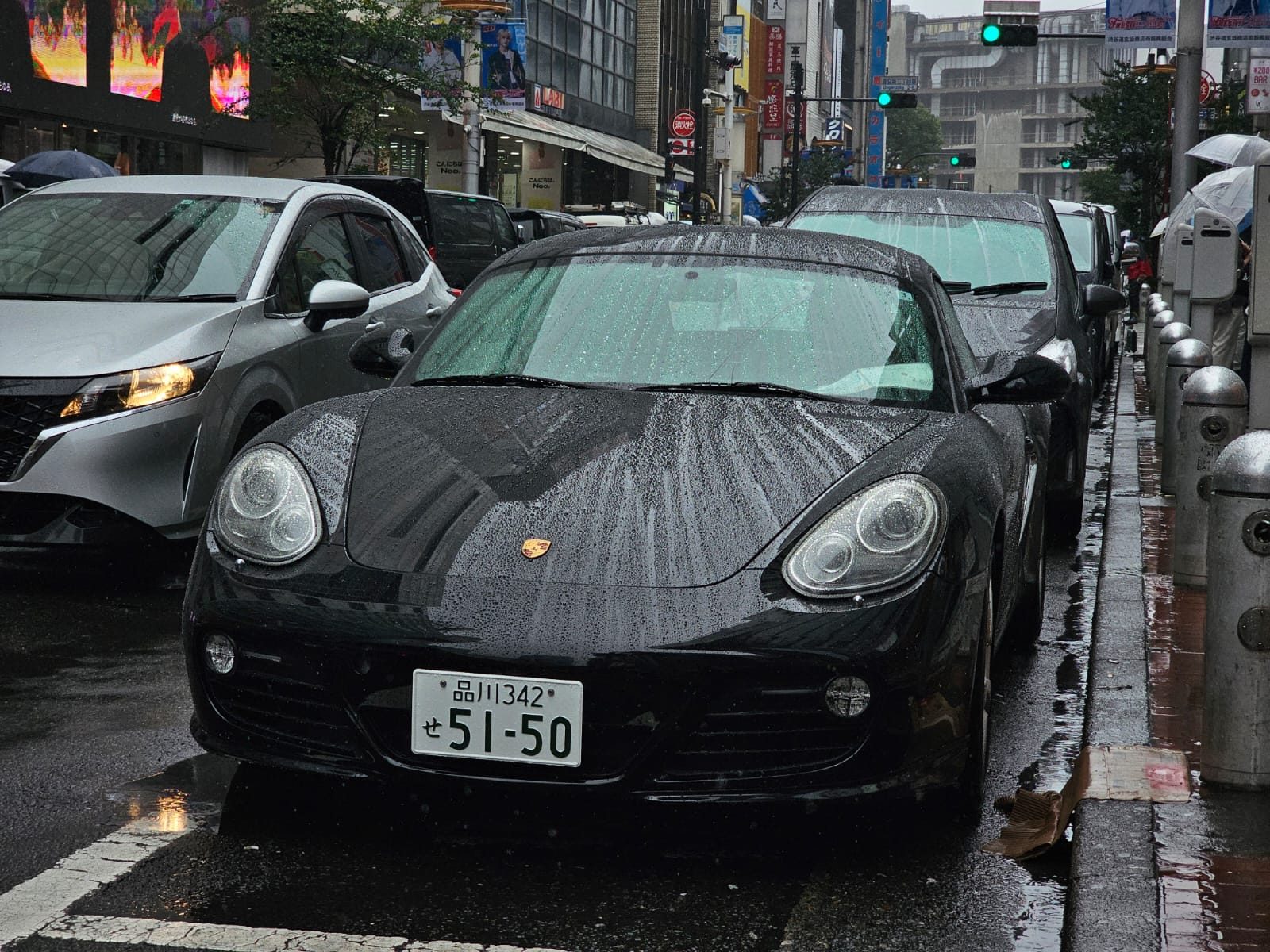 Black Porsche Cayman front end in heavy rain on a city street