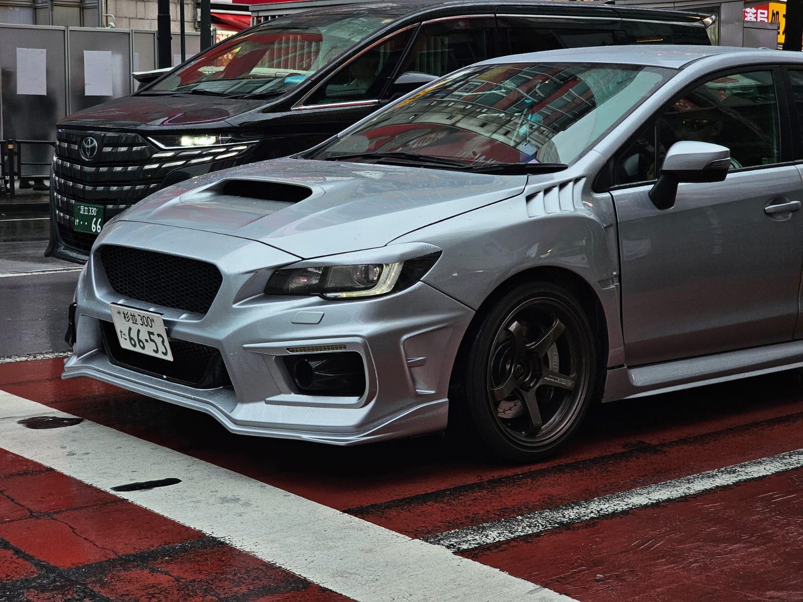 Silver Subaru WRX front end on a rainy red-painted crosswalk