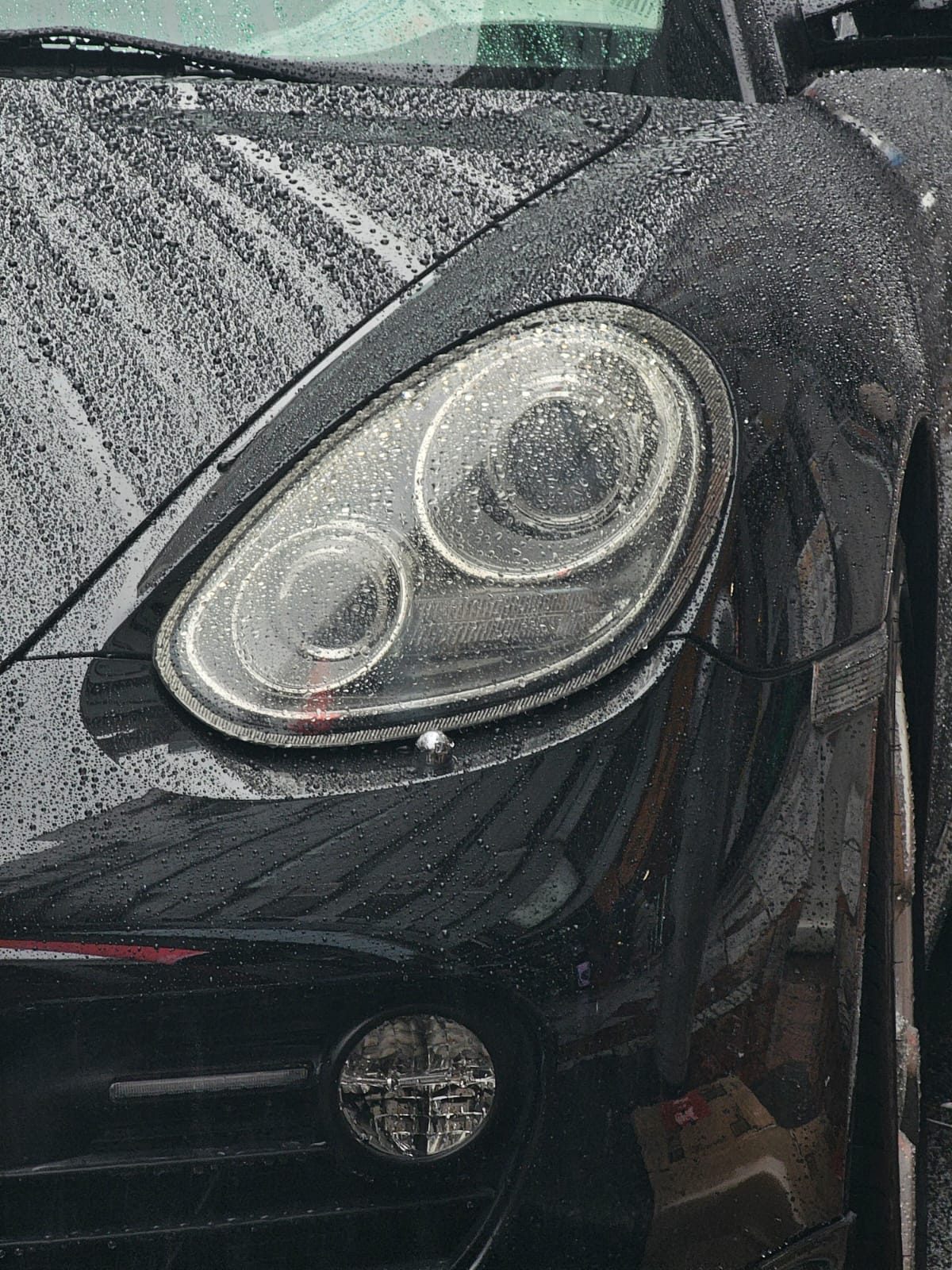 Close-up of a rain-covered Porsche Cayman headlight