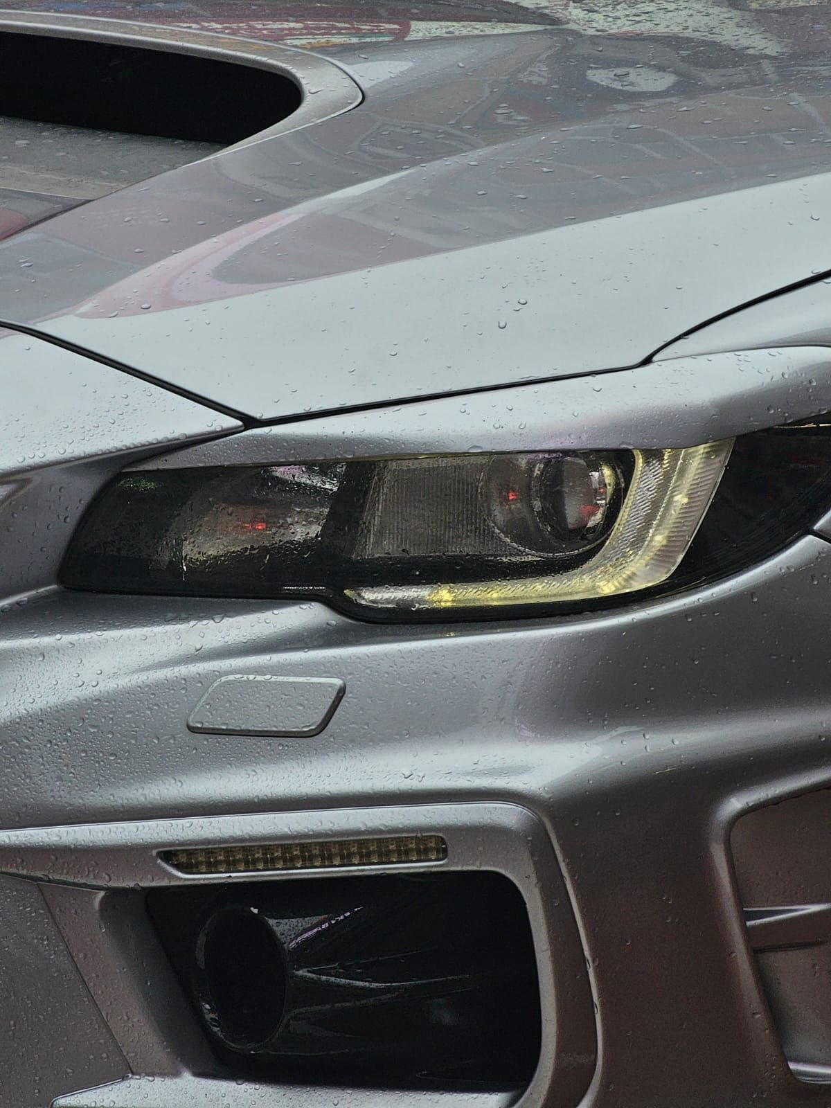 Close-up of a rain-covered car headlight with an amber accent strip