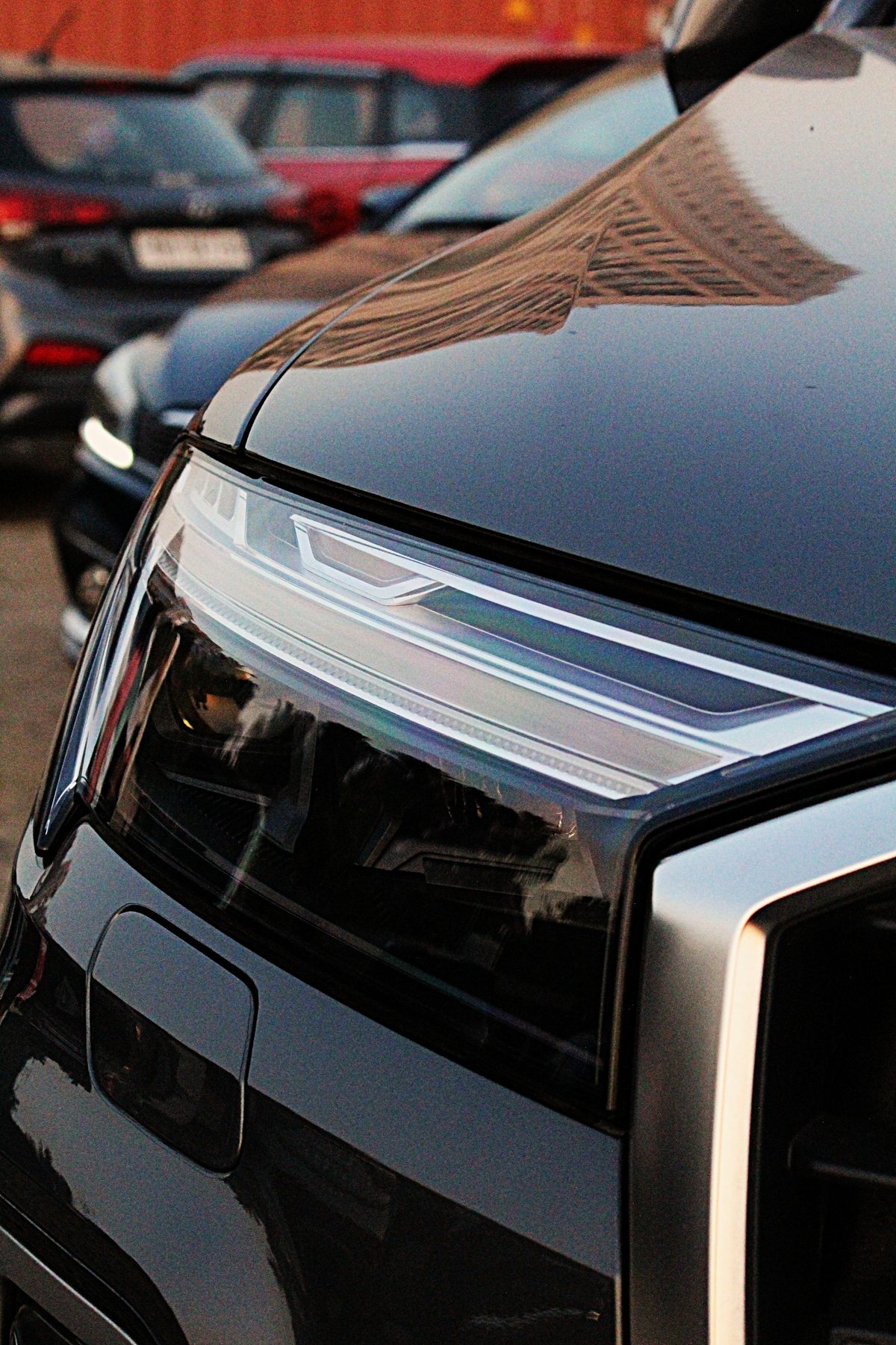 Close-up of a black Audi's headlight and greenhouse reflection in a parking lot