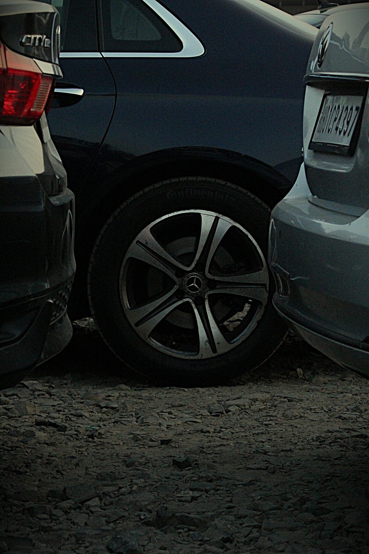 Mercedes-Benz wheel between two parked cars at dusk